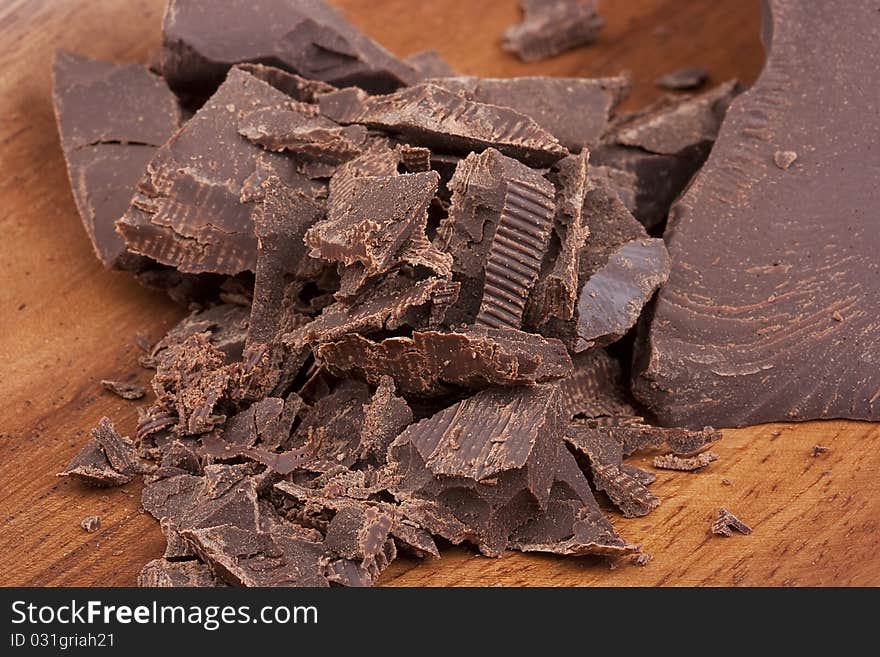 Bitter chocolate in pieces on a brown background in a plate.