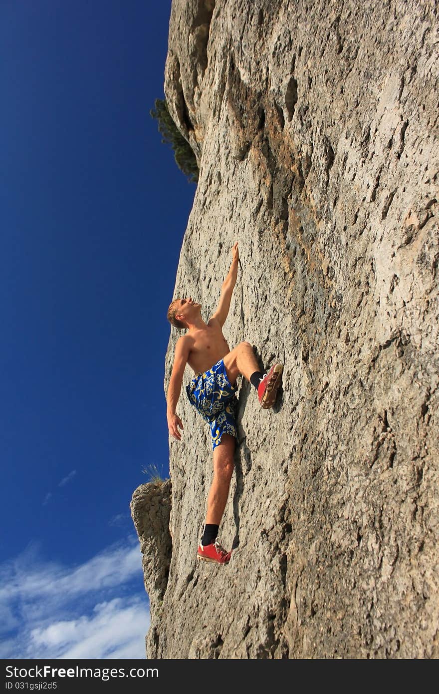 A guy climbs on a rock against the blue sky. A guy climbs on a rock against the blue sky