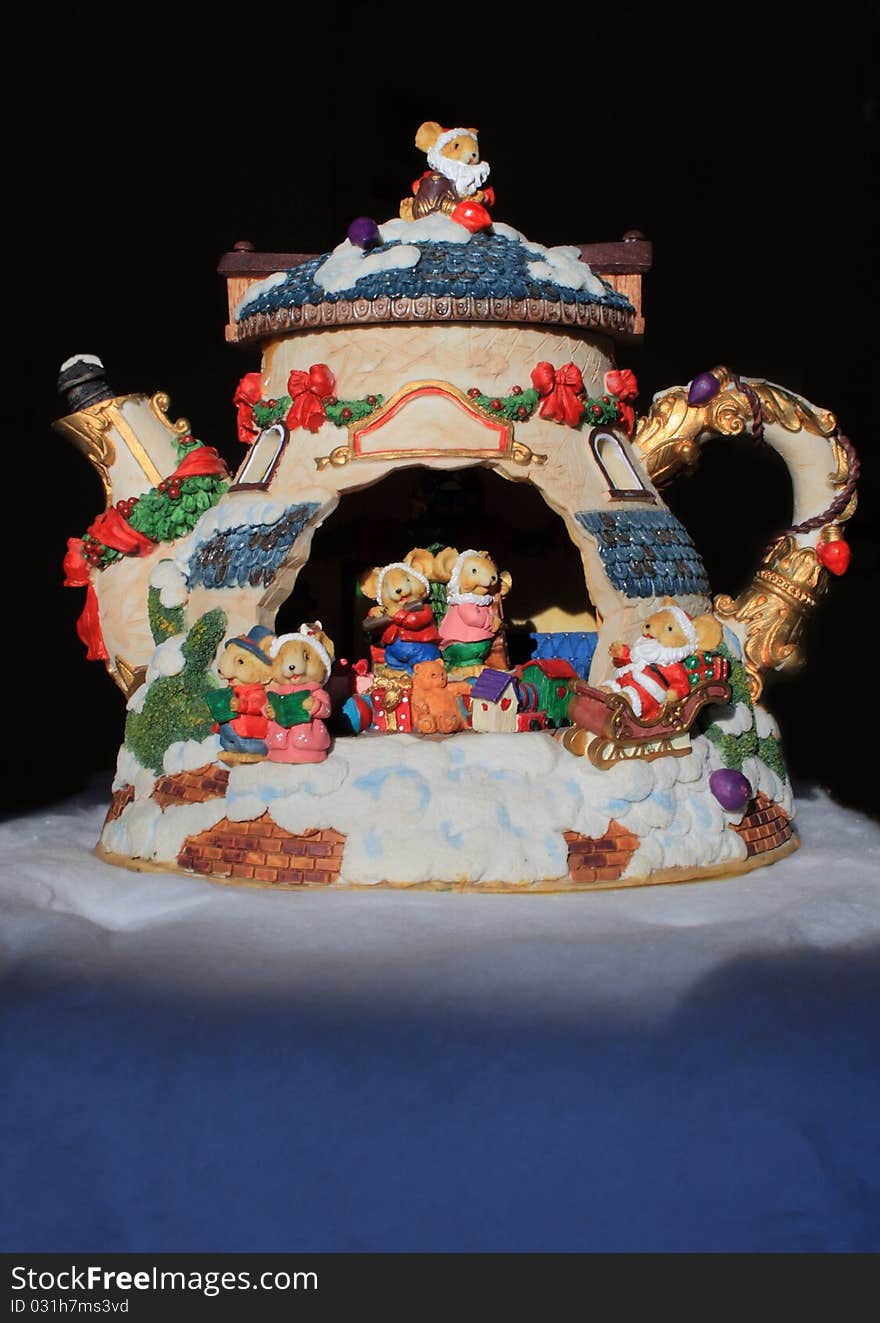 A colourful china teapot with miniature bear caricatures playing instruments and singing, surrounded by presents and toys. A colourful china teapot with miniature bear caricatures playing instruments and singing, surrounded by presents and toys.