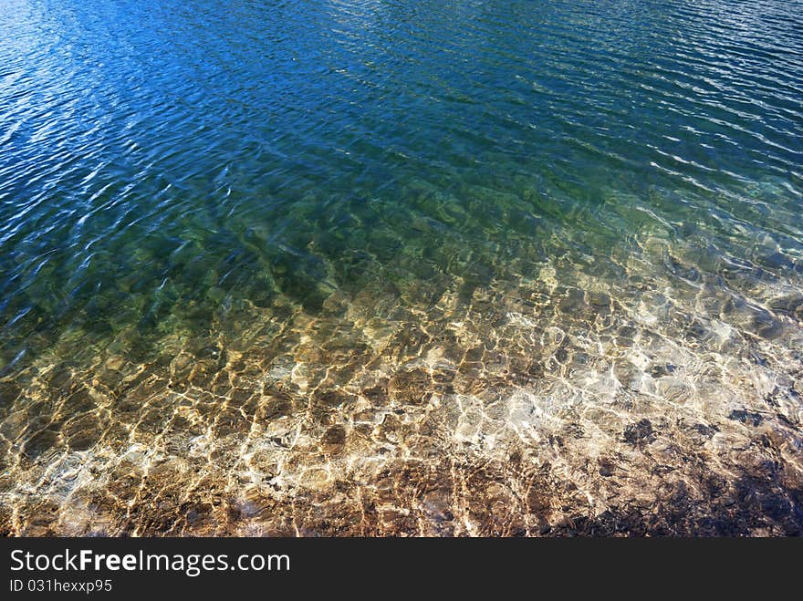 Looking into the water of a clear mountain lake with the blue sky reflected off the ripples in the water. Looking into the water of a clear mountain lake with the blue sky reflected off the ripples in the water.