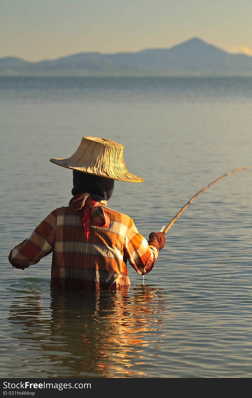 Thai woman fishing in the sea at sunset wearing traditional clothing and hat