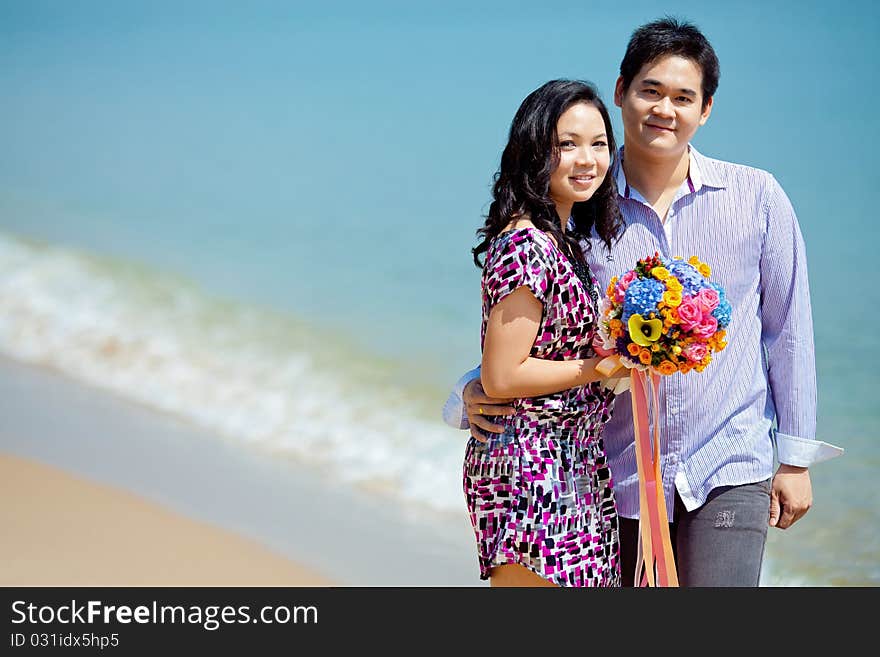 Attractive couple standing together on the beach with beautiful bouquet