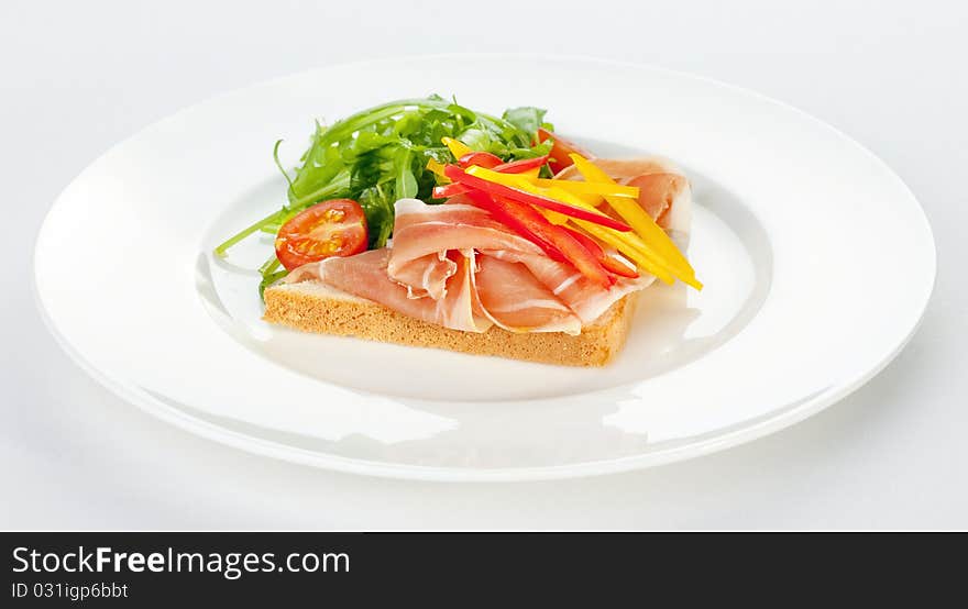 Sandwich with ham, tomatoes, paprika and ruccola on a white plate