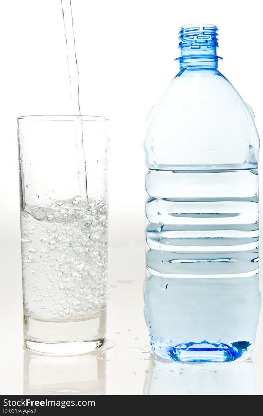 A bottle of fresh mineral water and a glass which is poured the same water on a white background