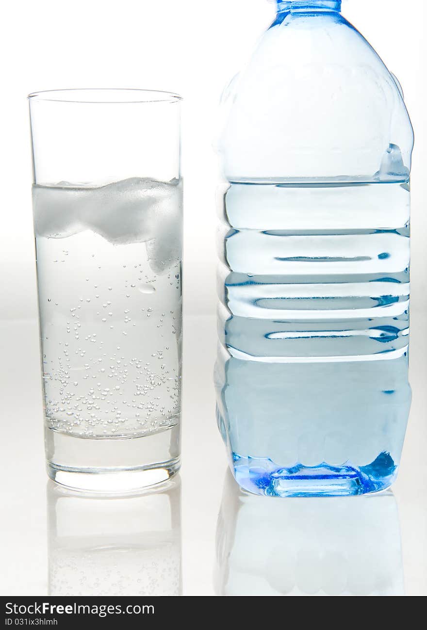 A bottle of fresh mineral water and a glass which is poured the same water on a white background