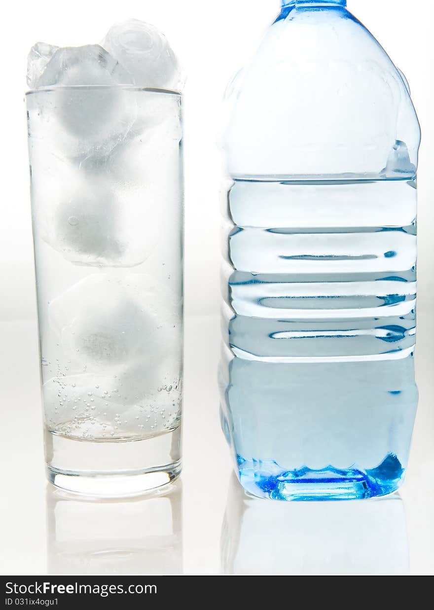 A bottle of fresh mineral water and a glass which is poured the same water on a white background