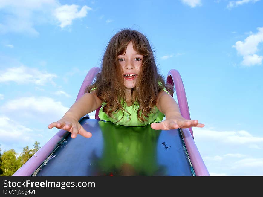 The girl lays on a children's hill having extended hands forward in the summer against the sky. The girl lays on a children's hill having extended hands forward in the summer against the sky