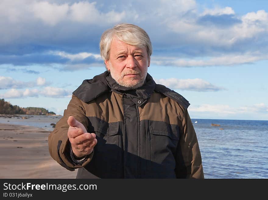 Mature poor man with grey hair at the Baltic sea asks for help in autumn day. Mature poor man with grey hair at the Baltic sea asks for help in autumn day.