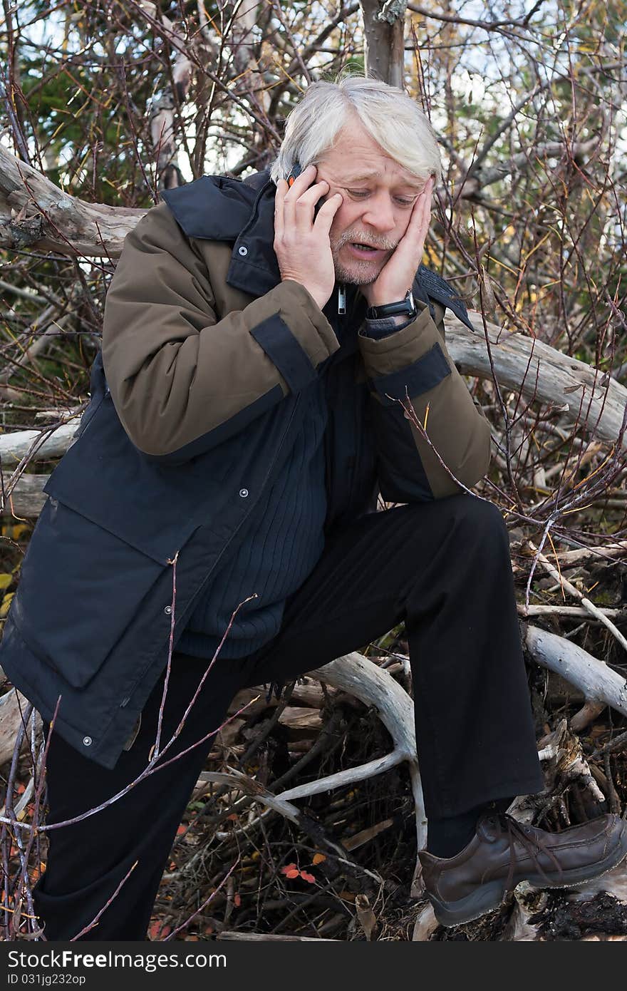 Mature busy man with grey hair in forest talking on the phone in autumn day. Mature busy man with grey hair in forest talking on the phone in autumn day.