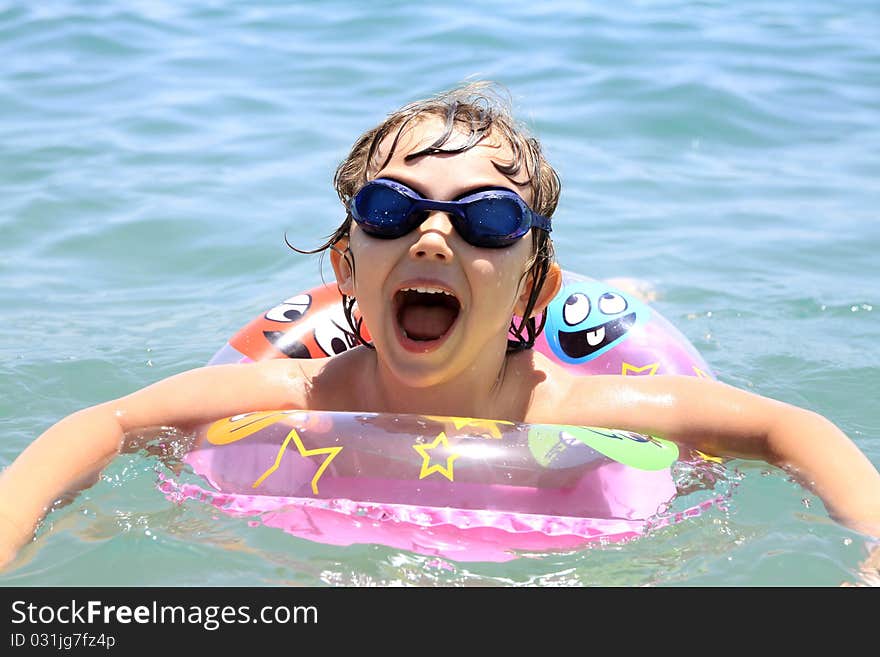 A small child swims in the sea. The girl in the pink circle swims and swimming glasses. Summer