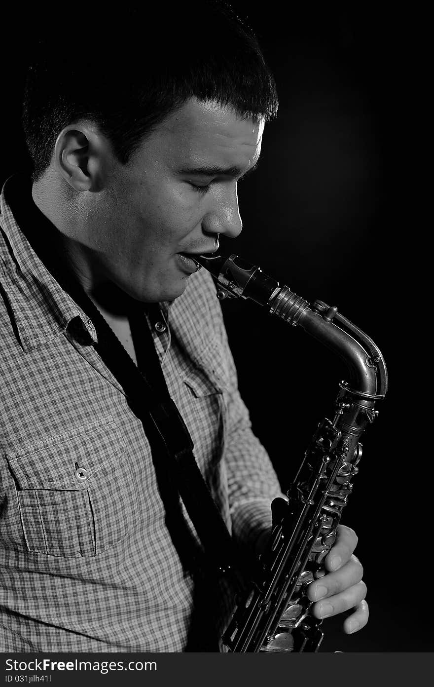 Young handsome man playing music on saxophone. black background