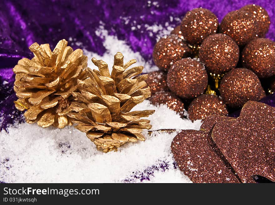 Christmas gold cones with brown balls on the snow and on violet background. Christmas gold cones with brown balls on the snow and on violet background.