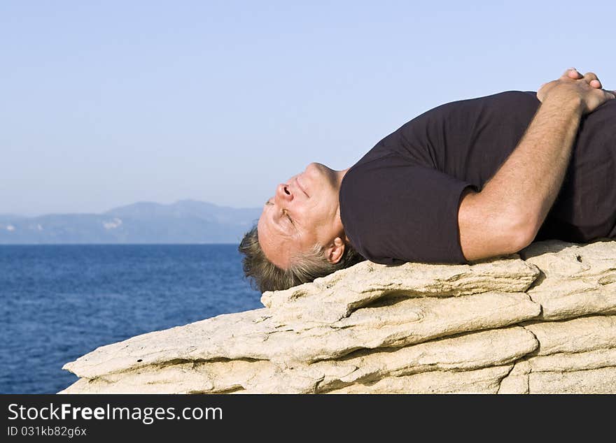 Color landscape photo of a mature man laying on a rock and sunbathing on the island of Paxos in the Ionian region of Greece. Color landscape photo of a mature man laying on a rock and sunbathing on the island of Paxos in the Ionian region of Greece.