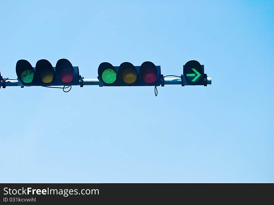 Green color on the traffic light on the blue sky background