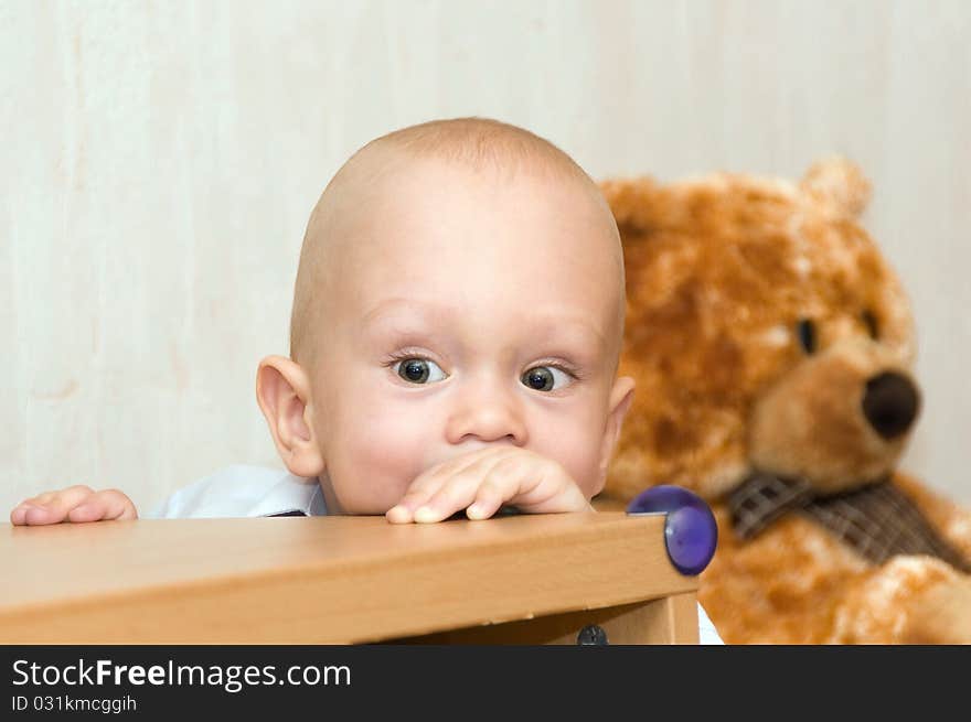 The small child playing looks out because of a table. The small child playing looks out because of a table