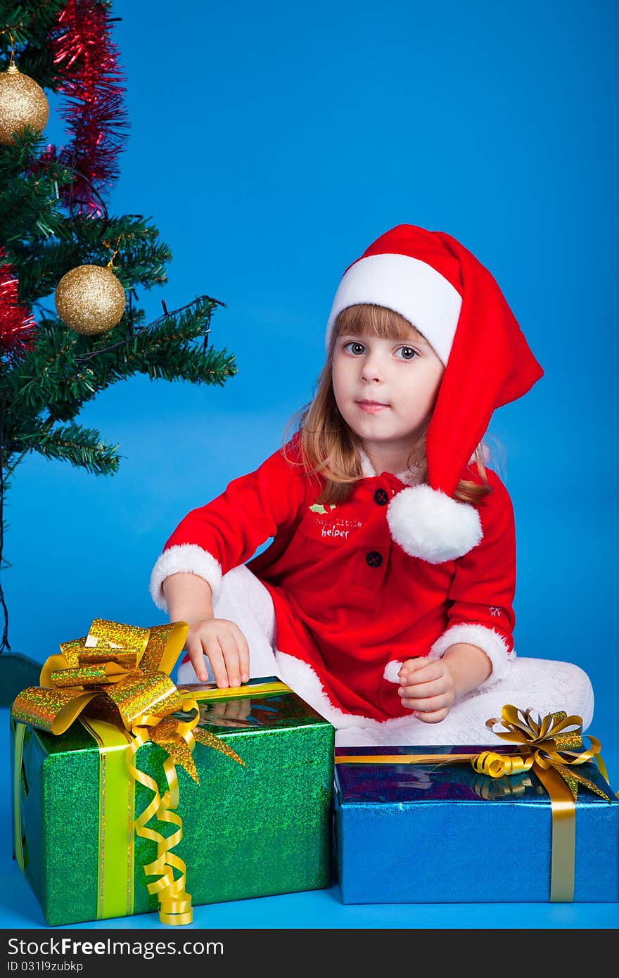 Pretty baby miss Santa sitting near Christmas tree