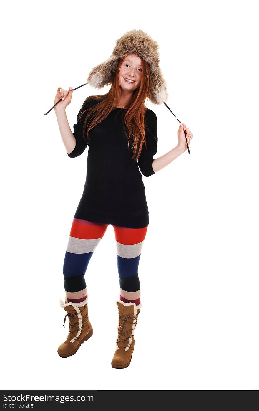 A pretty woman with long red hair in colorful tights, a black sweater and a fur hat and brown boots smiling for a portrait for white background. A pretty woman with long red hair in colorful tights, a black sweater and a fur hat and brown boots smiling for a portrait for white background.