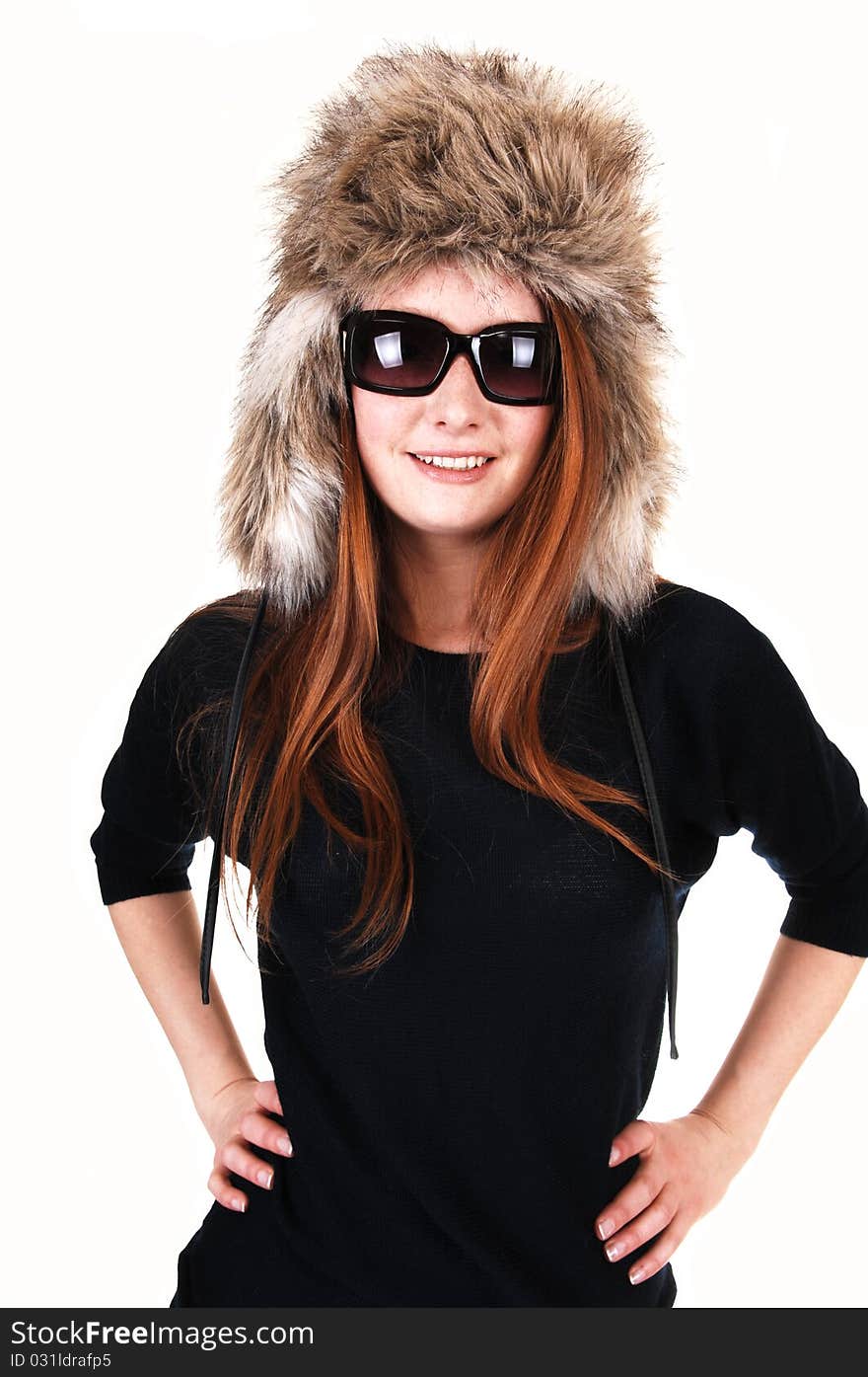 The portrait of a young woman with long red hair, sunglasses and a fur hat and a black sweater smiling into the camera, over white. The portrait of a young woman with long red hair, sunglasses and a fur hat and a black sweater smiling into the camera, over white.