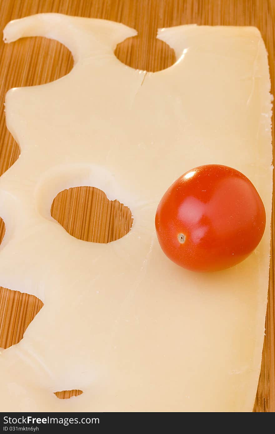 Swiss cheese slice and red tomato on a wood desk.