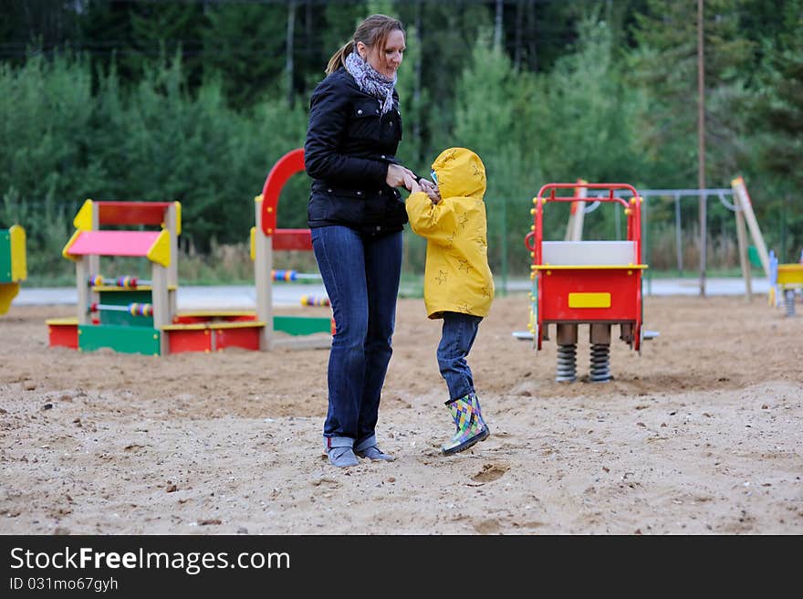 Mother plays with daughter on playground in cool autumn day