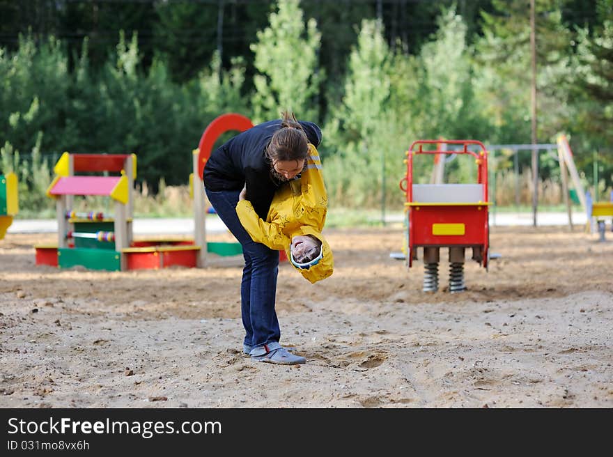 Mother plays with daughter on playground in cool autumn day