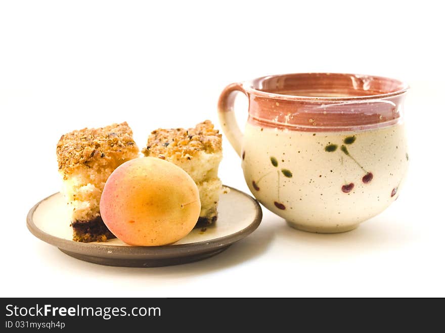 A cup of milk and a plate on which lay pieces of cake and a ripe apricot, on a white background. A cup of milk and a plate on which lay pieces of cake and a ripe apricot, on a white background