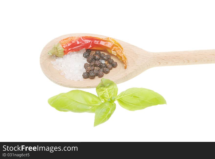 Chilli pepper, salt and pepper in a wooden spoon with fresh basil leaves on white. Chilli pepper, salt and pepper in a wooden spoon with fresh basil leaves on white