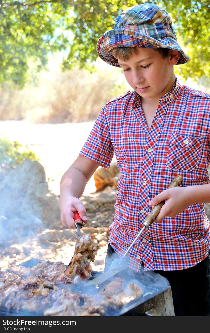 Teenager in a park on a holiday to cook meat and steaks on the grill. Teenager in a park on a holiday to cook meat and steaks on the grill