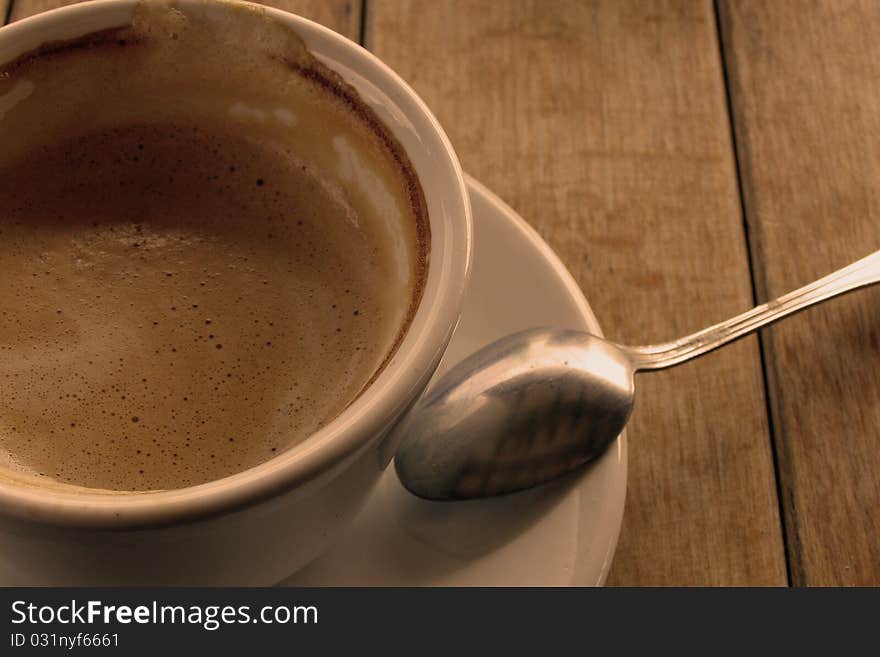 Having a cup of coffee concept; closeup image of a coffee in a white cup and saucer, with a teaspoon, isolated on a wooden table