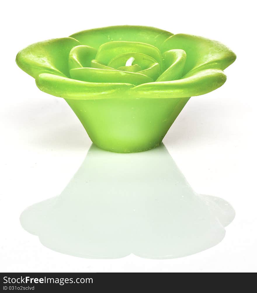 A green candle shaped as a rose sits against a white background with a reflection. A green candle shaped as a rose sits against a white background with a reflection