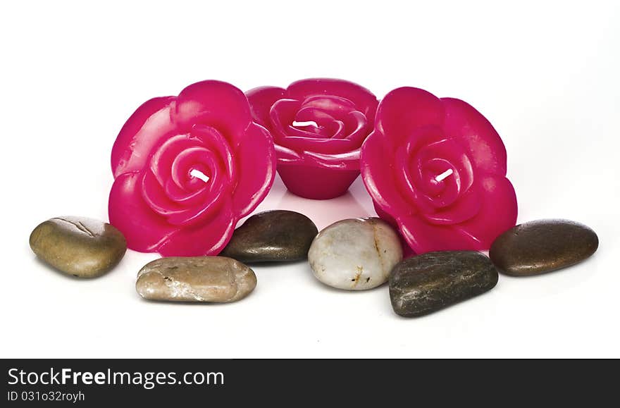 Red rose shaped candles sit against a white background with spa rocks. Red rose shaped candles sit against a white background with spa rocks