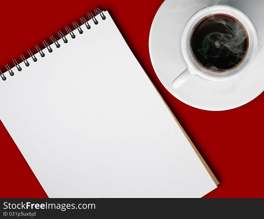 White cup of hot coffee and notebook on red table background