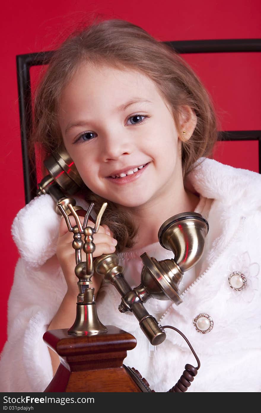 Portrait of a celebatory dressed cute smiley little girl talkin by an old phone. Portrait of a celebatory dressed cute smiley little girl talkin by an old phone