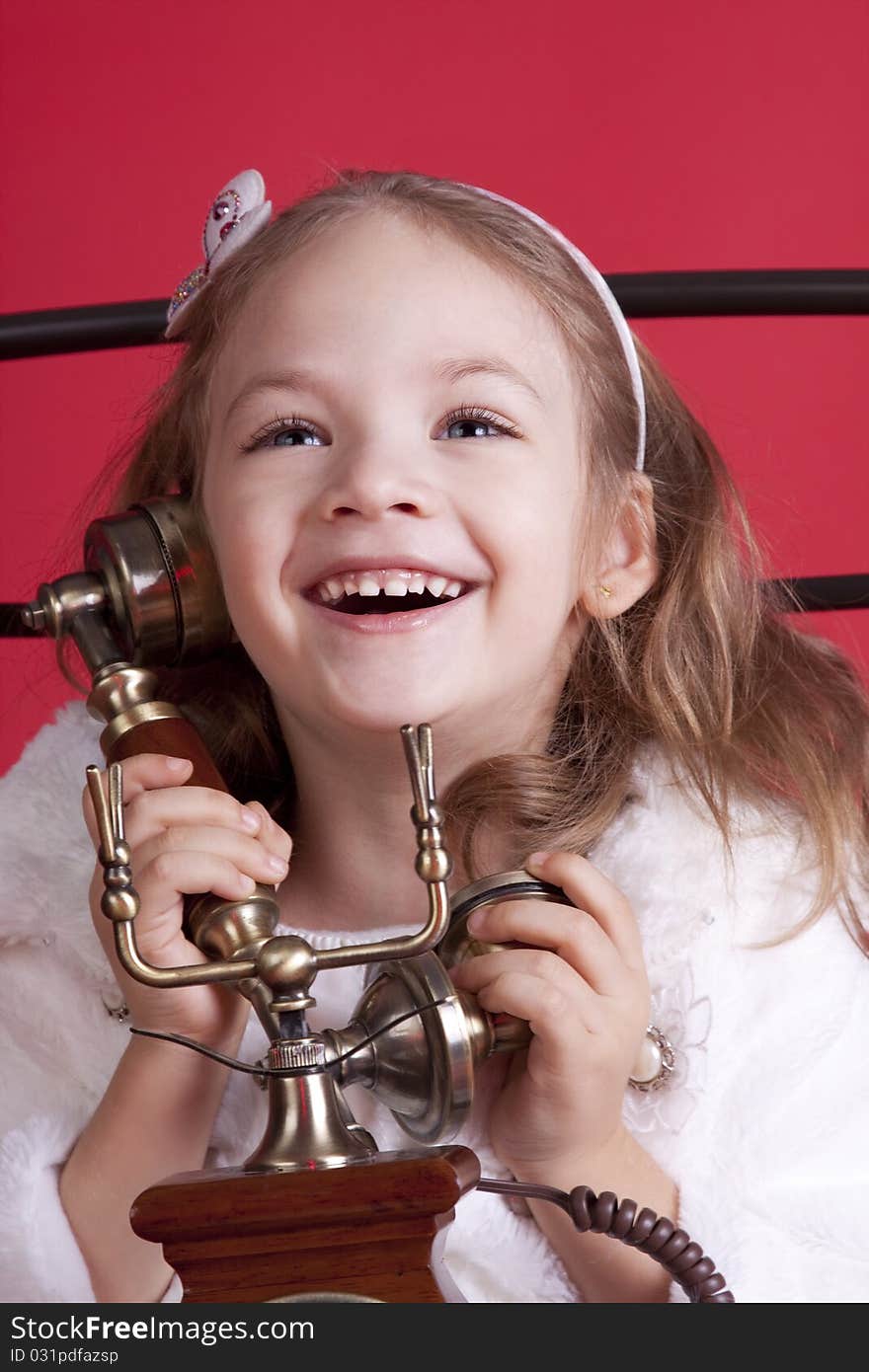 Portrait of a celebatory dressed cute happy little girl talkin by an old phone. Portrait of a celebatory dressed cute happy little girl talkin by an old phone