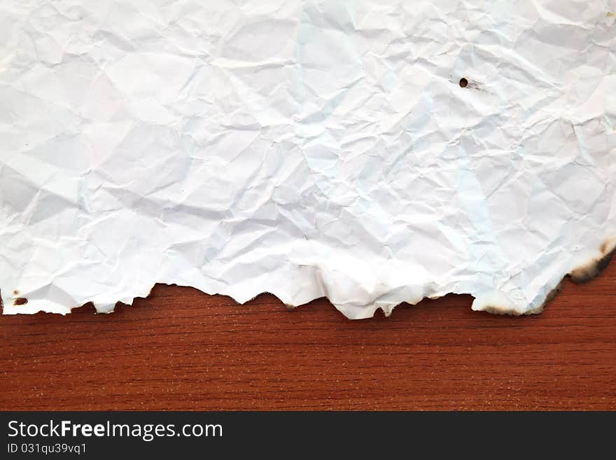 Wrinkled paper with burnt edges on wooden board