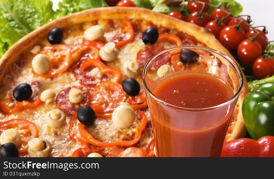 Closeup picture of a pizza with vegetables and glass of tomato juice