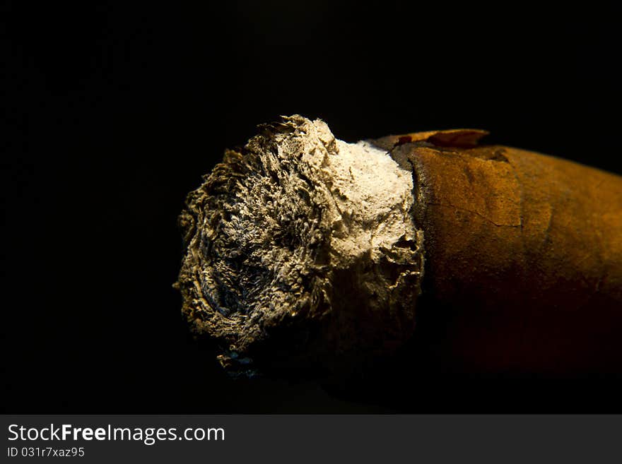 Used cigar with its ash at the front, lit from above on black background. Used cigar with its ash at the front, lit from above on black background.