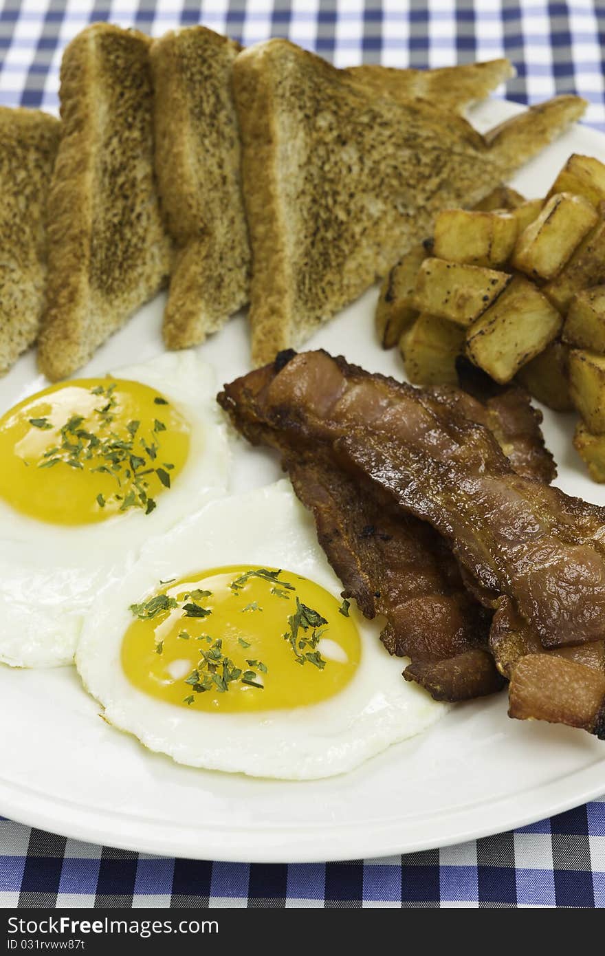 Breakfast meal on a white plate with two eggs,potato,toasted bread and bacon. Orientation : vertical Concept : mealtime,food,morning. Breakfast meal on a white plate with two eggs,potato,toasted bread and bacon. Orientation : vertical Concept : mealtime,food,morning