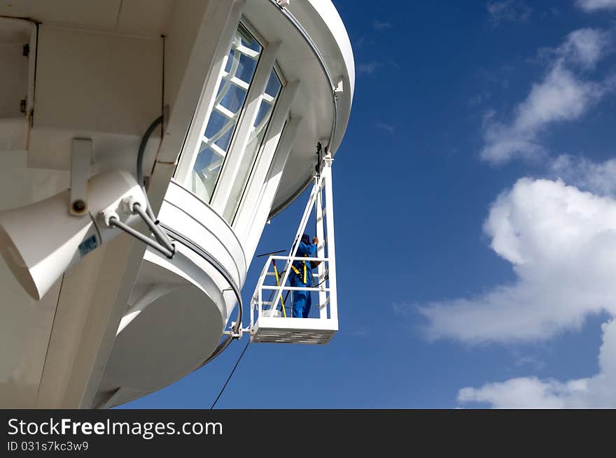 Worker cleaning windows on a cruise ship while teathered for safety. Worker cleaning windows on a cruise ship while teathered for safety.