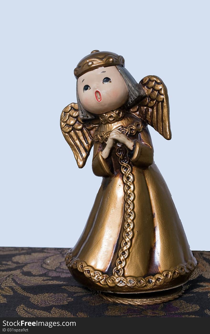 Antique Christmas angel music box, standing on black patterned cloth, with white background. The angel is singing, wearing a halo or crown, and has wings. Antique Christmas angel music box, standing on black patterned cloth, with white background. The angel is singing, wearing a halo or crown, and has wings.