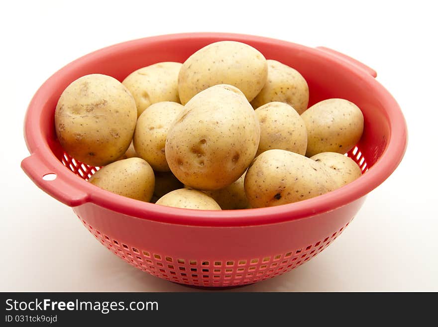 Raw potatoes in the red kitchen sieve. Raw potatoes in the red kitchen sieve