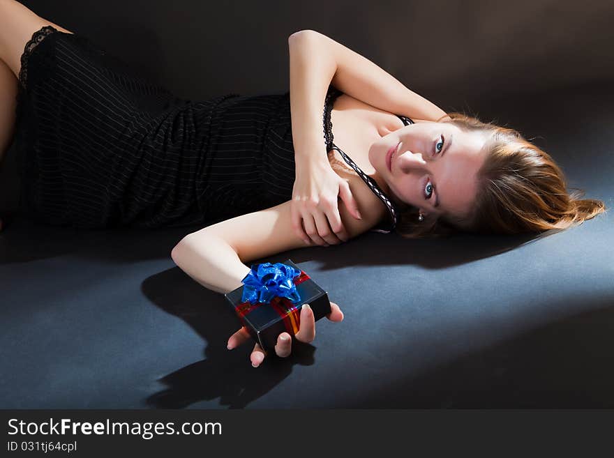 Girl with a gift in a hand lies against a dark background. Girl with a gift in a hand lies against a dark background