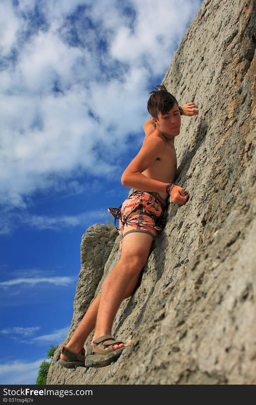 A guy climbs on a rock against the blue sky. A guy climbs on a rock against the blue sky