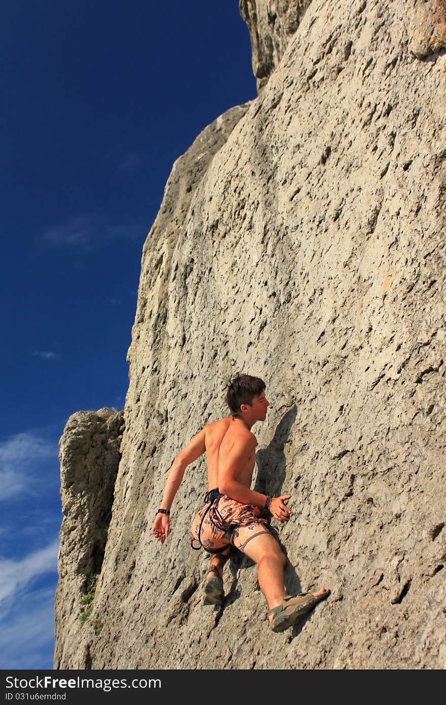 A guy climbs on a rock against the blue sky. A guy climbs on a rock against the blue sky