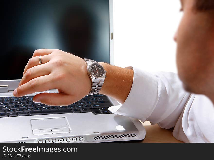 The young worker of office looks at the watch at the computer on a workplace. The young worker of office looks at the watch at the computer on a workplace