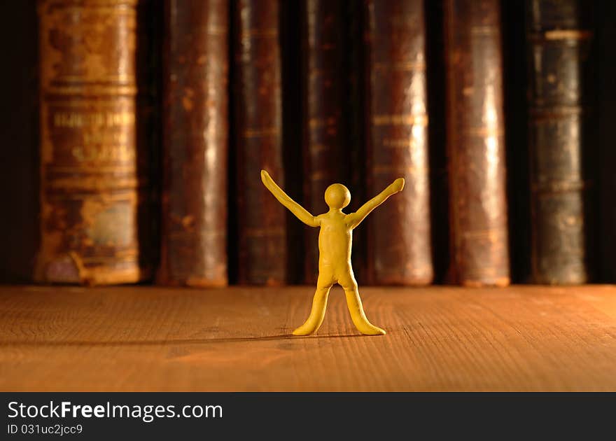 Small yellow plasticine man standing on background with old books in a row. Small yellow plasticine man standing on background with old books in a row