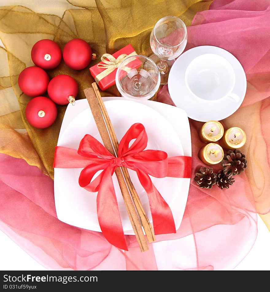 Christmas table-a plate decorated with cinnamon sticks and ribbon, a cup, glasses, christmas balls, candles, gift and cones