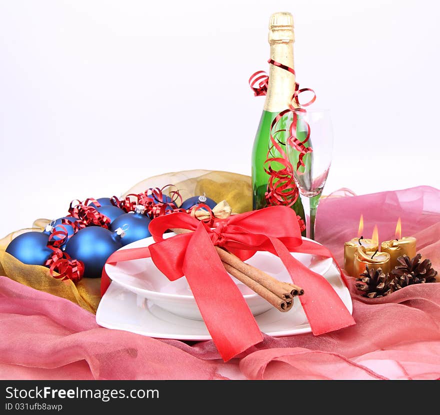 Christmas or New Year's setting - a plate decorated with ribbon and cinnamon sticks, a bottle of champagne, a glass, candles, christmas balls