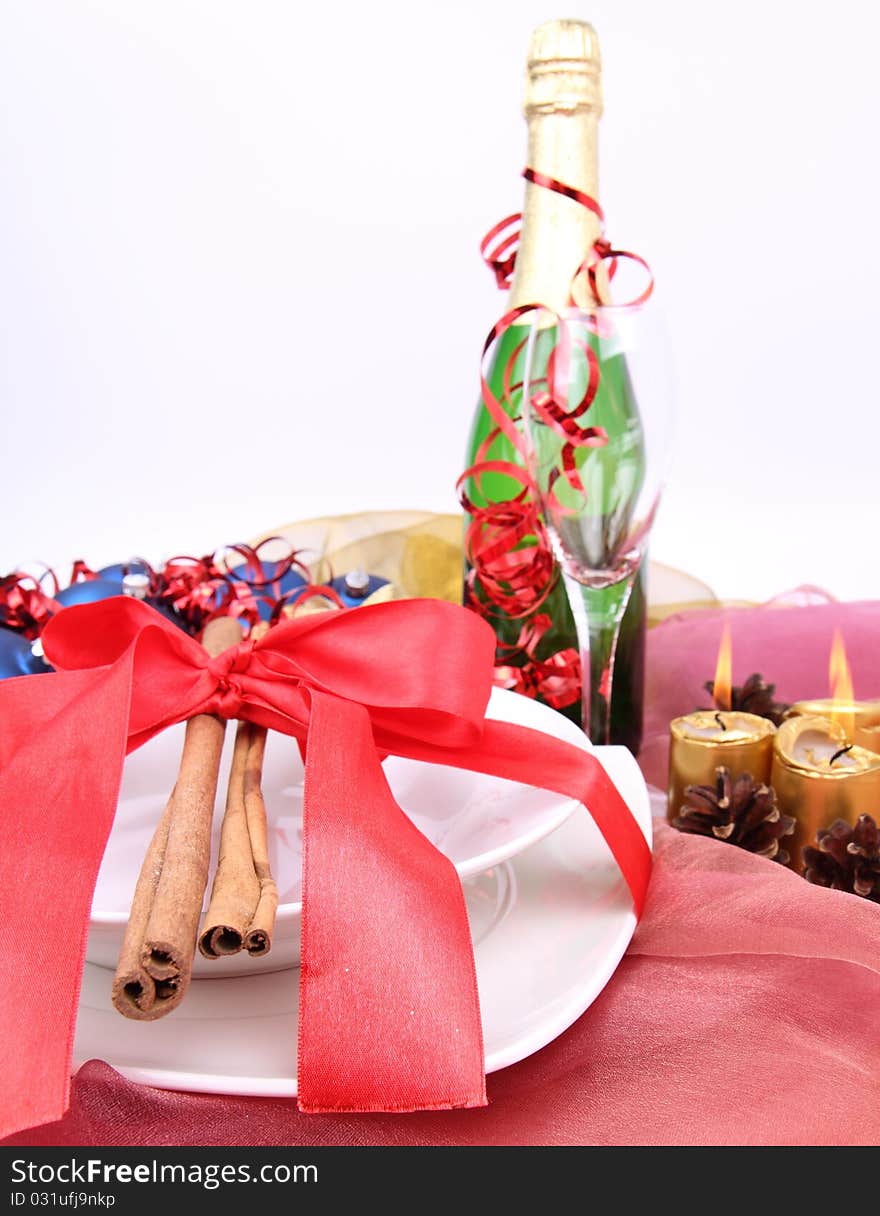 New Year's or Christmas setting - a plate decorated with ribbon and cinnamon sticks, a bottle of champagne, a glass, candles, a gift , cones, christmas ball