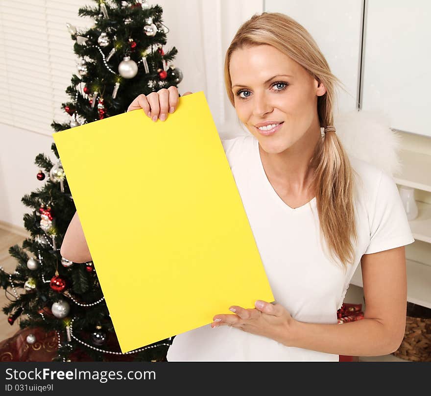 Beautiful blond angel standing next to a christmas tree holding a sign. Beautiful blond angel standing next to a christmas tree holding a sign